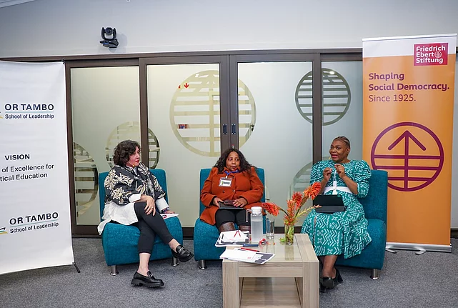 Three women sit on a panel at the OR Tambo School of Leadership. The speaker on the right gestures while speaking. A Friedrich-Ebert-Stiftung banner reading “Shaping Social Democracy. Since 1925.” stands behind the panel.
